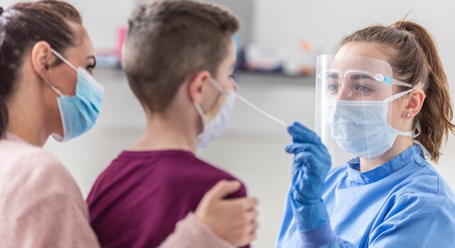 mom_holds_her_son_as_medical_worker_takes_sample_from_his_nose_during_coronavirus_pandemic_testing